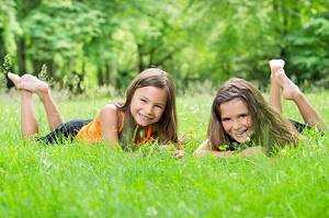 Kinder lachen in die Kamera auf einem Landschaftsrasen liegend